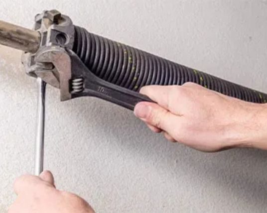 A technician safely replacing a broken torsion spring on a residential garage door in Roswell GA.